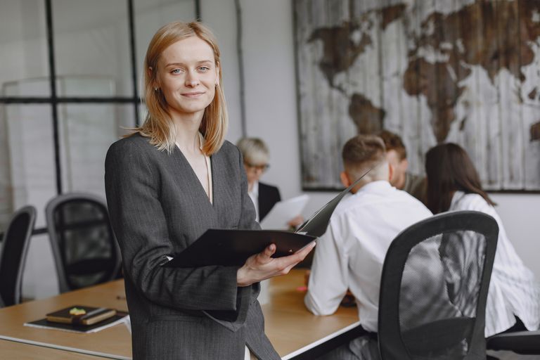 Confident businesswoman holding folder during a team meeting in modern office setting.