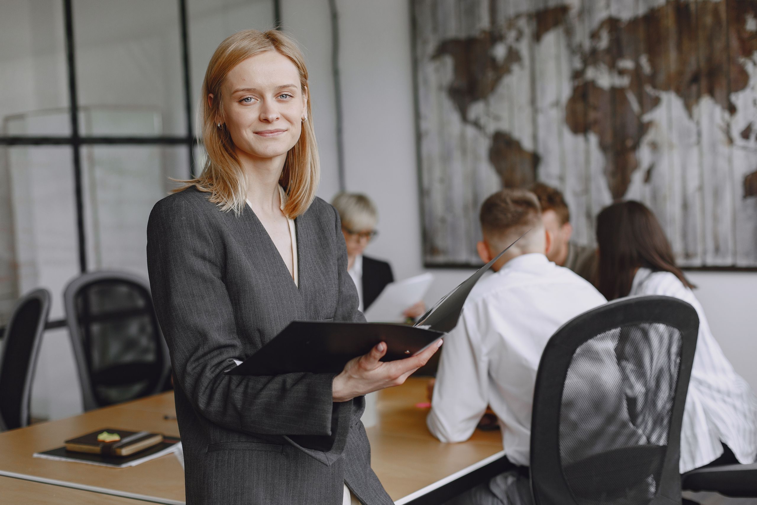 Confident businesswoman holding folder during a team meeting in modern office setting.